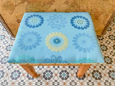 A small wooden stool with a blue floral patterned cushion on tiled floor and a map in the background at Down the Rabbit Hole in Brinsea near Congresbury