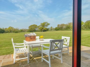 A white outdoor dining table with four chairs on a stone patio overlooking a green field at Down the Rabbit Hole Brinsea near Congresbury