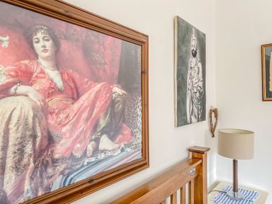 A bedroom wall with framed paintings above a wooden headboard and a lamp on a bedside table at Down the Rabbit Hole Brinsea near Congresbury