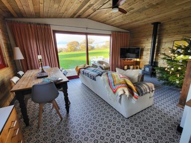 A living room with a wooden dining table and chairs a white sofa with colorful blankets a wood stove and a decorated Christmas tree at Down the Rabbit Hole Brinsea near Congresbury