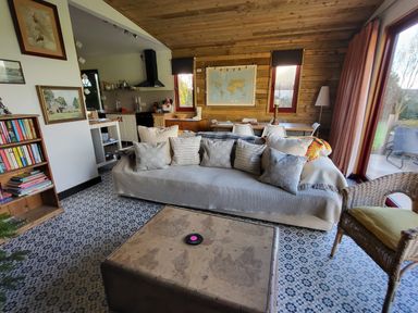 A living room with a sofa and cushions a coffee table a bookshelf and a kitchen area at Down the Rabbit Hole in Brinsea near Congresbury