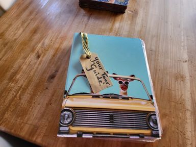 A wooden table with a booklet showing two giraffes in a yellow car with a tag reading Your Tour Guide down the rabbit hole in Brinsea near Congresbury