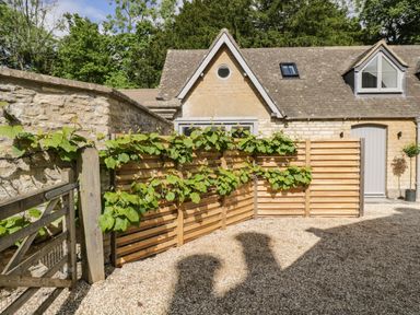 A stone house with a wooden gate and wooden fence with plants at The Hayloft in Sherston