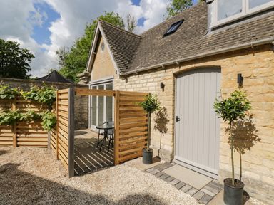 A stone cottage exterior with a small fenced patio and two potted plants at The Hayloft in Sherston