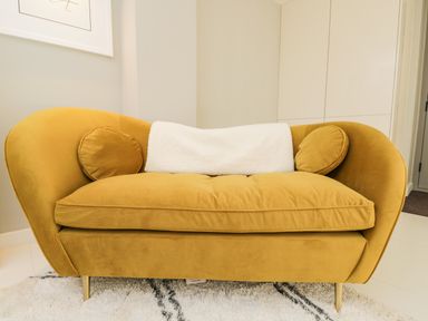 A mustard yellow sofa with two round cushions and a white throw blanket on a rug in a room