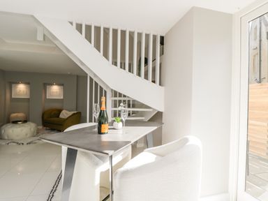 A dining area with a table set with champagne and glasses near white chairs and a white staircase at The Hayloft in Sherston