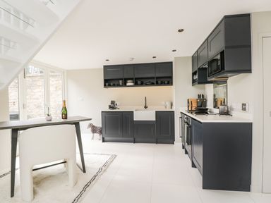 A modern kitchen with black cabinets white countertops a wooden table and a white chair at The Hayloft in Sherston