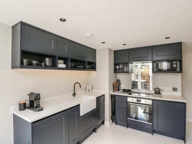 A kitchen with dark grey cabinets a white countertop a sink a coffee machine an oven and a microwave at The Hayloft in Sherston