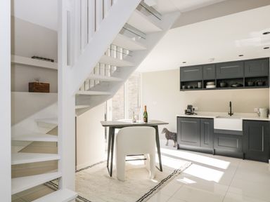 A kitchen with black cabinets a white sink and a dining table under a staircase at The Hayloft in Sherston