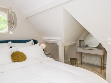 A bedroom with a bed with white linens and round mustard pillow near a dressing table with a round mirror at The Hayloft in Sherston