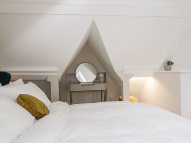 A bedroom with a bed and pillows a small table with a round mirror and a plant at The Hayloft in Sherston
