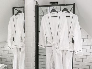 Two white bathrobes hanging on black hangers in a tiled bathroom at The Hayloft in Sherston