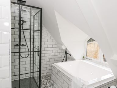 A bathroom with a glass shower enclosure and a bathtub under a slanted ceiling at The Hayloft in Sherston