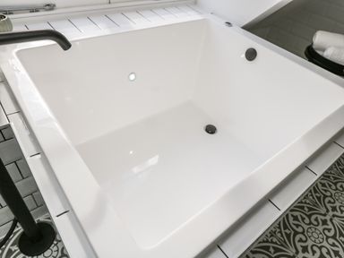 A white bathtub with black fixtures and patterned floor tiles at The Hayloft in Sherston