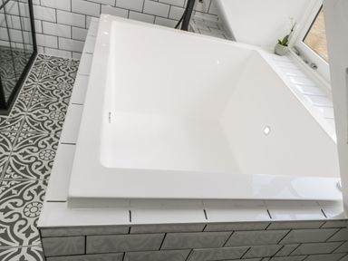 A white bathtub with white tiled surround next to a window and patterned floor tiles at The Hayloft in Sherston
