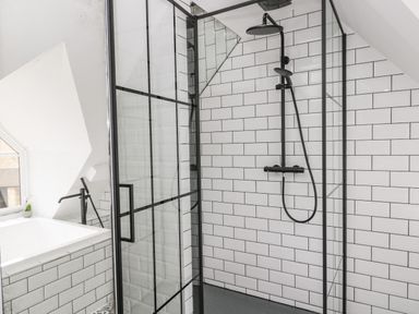 A bathroom with a glass shower enclosure with black fixtures and a bathtub next to a window at The Hayloft in Sherston