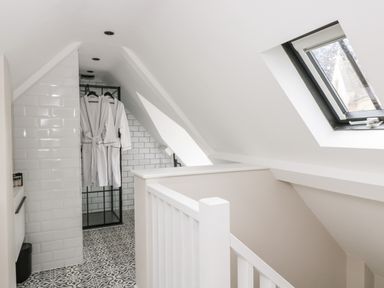 A bathroom with white tiled walls black framed shower two white robes hanging patterned floor tiles and a skylight window at The Hayloft in Sherston