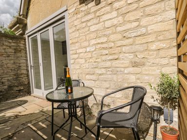 An outdoor patio area with a glass table bottle and glass two chairs and a potted plant at The Hayloft in Sherston