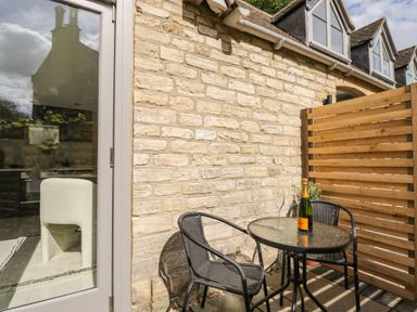 An outdoor patio area with a round glass table two black chairs a bottle of champagne and a glass at The Hayloft in Sherston