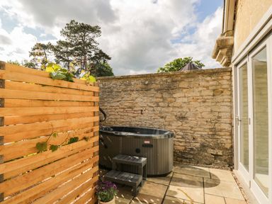 An outdoor patio area with a hot tub steps wooden fence and stone wall at The Hayloft in Sherston