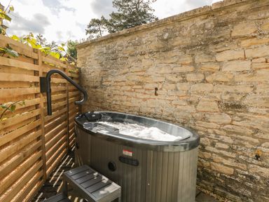 An outdoor hot tub with a step stool next to a stone wall and wooden fence at The Hayloft in Sherston