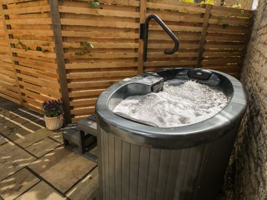 An outdoor hot tub with bubbling water next to a wooden fence and stone wall with a small set of steps and a potted plant