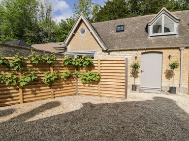 A stone building with a grey door and windows a wooden privacy fence with green plants and a gravel ground at The Hayloft in Sherston