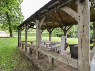 An outdoor wooden gazebo with a table and chairs set on a tiled floor in a grassy area at The Hayloft in Sherston