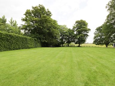 A large grassy lawn with trees and a hedge surrounding the area at The Hayloft in Sherston