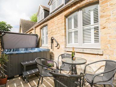 An outdoor patio with a hot tub table with a bottle and glasses and four chairs at The Coach House in Westonbirt near Tetbury