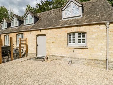 A stone cottage exterior with multiple dormer windows outdoor seating and a gravel area at The Coach House Westonbirt near Tetbury