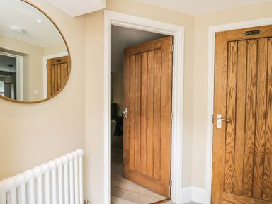 A hallway with two wooden doors one open and one labeled WC a round mirror and white radiator at The Coach House in Westonbirt near Tetbury