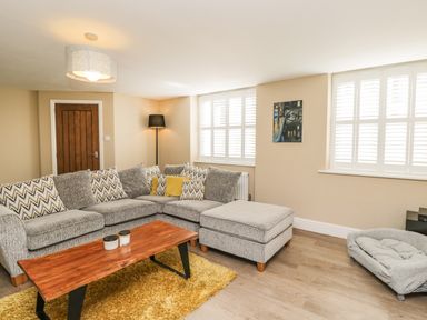 A living room with a grey sectional sofa coffee table and a floor lamp at The Coach House in Westonbirt near Tetbury