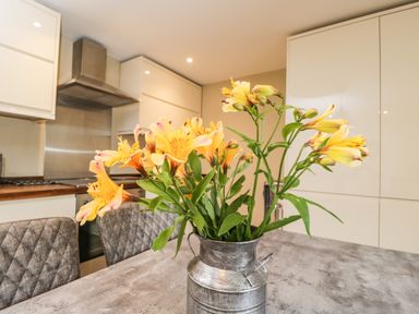 A kitchen with yellow flowers in a metal vase on a countertop and quilted chairs at The Coach House Westonbirt near Tetbury