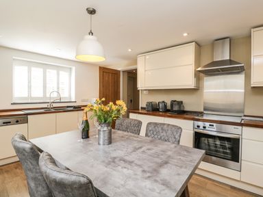 A kitchen with a dining table, chairs, stainless steel oven, and countertop appliances at The Coach House in Westonbirt near Tetbury
