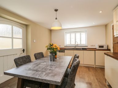 A kitchen with a dining table with chairs and flowers on the table at The Coach House in Westonbirt near Tetbury