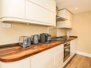 A kitchen with white cabinets wooden countertop a toaster kettle coffee machine oven and stovetop at The Coach House Westonbirt near Tetbury