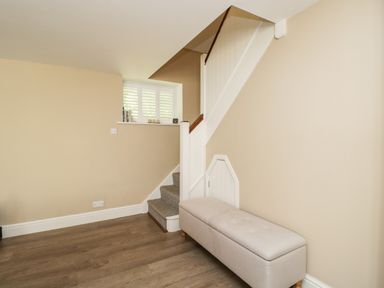 A stairway with carpeted steps beside a beige bench and a small door under the stairs at The Coach House in Westonbirt near Tetbury