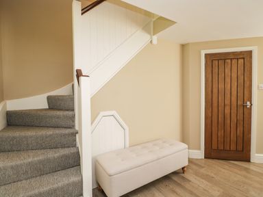 A hallway with carpeted stairs a wooden door and a beige upholstered bench at The Coach House in Westonbirt near Tetbury