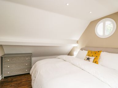 A bedroom with a bed white bedding a gray chest of drawers and a round window at The Coach House Westonbirt near Tetbury