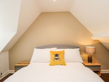 A bedroom with a bed with white bedding yellow pillow with bee design and a lamp on a bedside table at The Coach House in Westonbirt near Tetbury