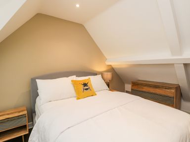 A bedroom with a bed white bedding a yellow pillow two wooden bedside tables and a lamp at The Coach House in Westonbirt near Tetbury