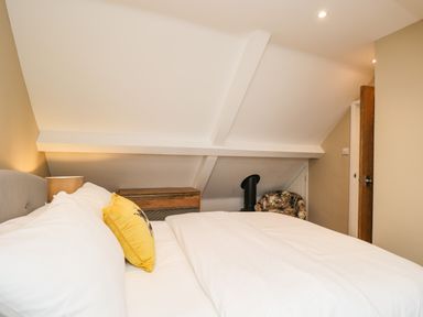 A bedroom with a bed a yellow pillow a bedside lamp a wooden chest and a floral chair at The Coach House Westonbirt near Tetbury