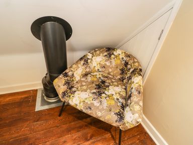 A floral patterned armchair next to a black stove pipe on a wooden floor at The Coach House Westonbirt near Tetbury