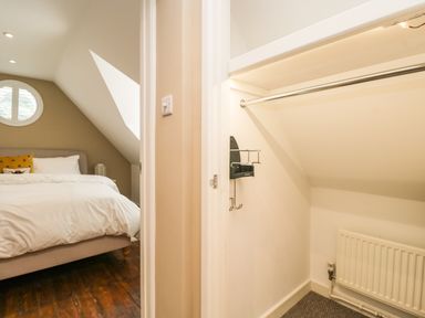 A small bedroom with a bed and a window next to a closet with a hanging rod and radiator at The Coach House Westonbirt near Tetbury