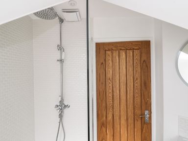 A shower area with a rain showerhead and a wooden door in a bathroom at The Coach House in Westonbirt near Tetbury