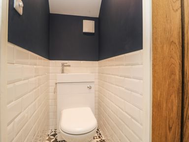 A small bathroom with a white toilet and sink combination with white tiled walls and dark upper walls at The Coach House Westonbirt near Tetbury