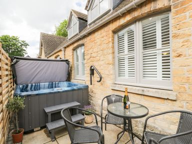 An outdoor patio with a hot tub table with a champagne bottle and glasses and three chairs at The Coach House in Westonbirt near Tetbury