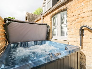 An outdoor hot tub with bubbling water next to a stone wall and window at The Coach House in Westonbirt near Tetbury