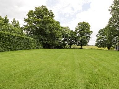 A large green lawn surrounded by trees and a hedge at The Coach House in Westonbirt near Tetbury